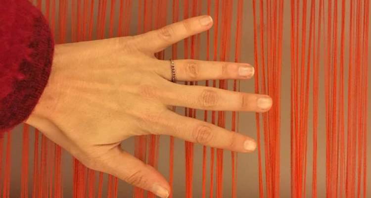 Una mano di donna poggiata su fili di lana per la tessitura al telaio. L'Umbria che non ti aspetti