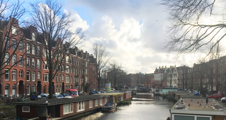 Canale di Amsterdam sovrastato da cielo azzurro e poche nuvole bianche