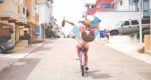 Ragazza in bicicletta con spumante e palloncini